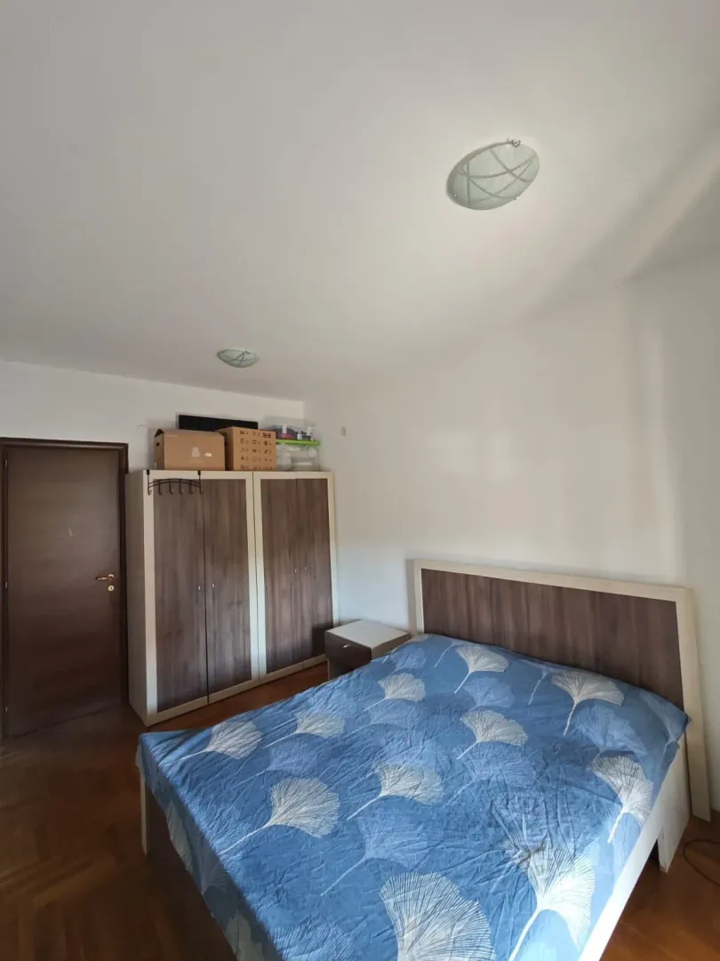 Spavaća soba sa bračnim krevetom, ormarom i drvenim podom.