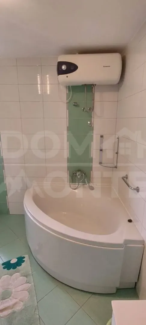 Manje kupatilo sa ugaonom kadom i bojlerom na zidu.