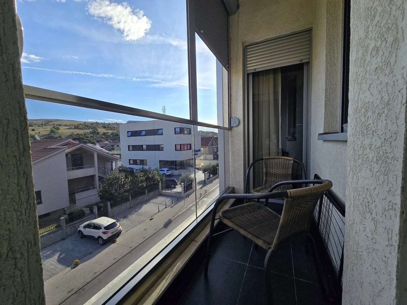 Manji namješten balkon sa staklenom ogradom i pogledom na ulicu.