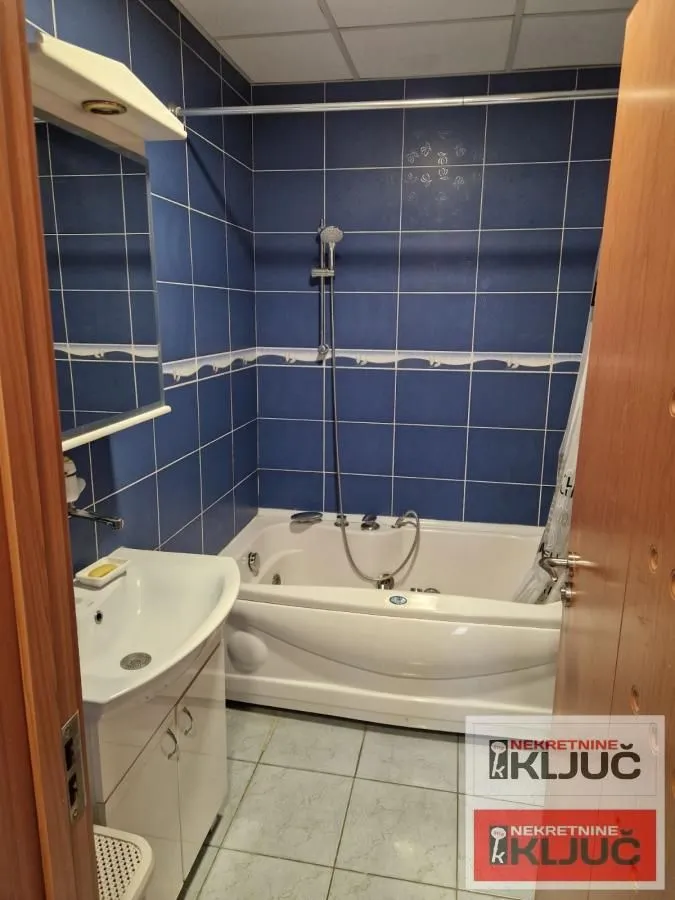 Kupatilo sa kadom, umivaonikom i plavim zidnim pločicama.