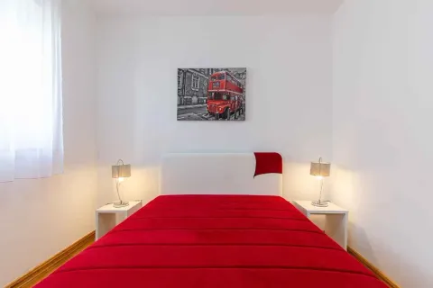 Spavaća soba sa bračnim krevetom, noćnim stočićima i umjetničkom slikom na zidu. - image 13