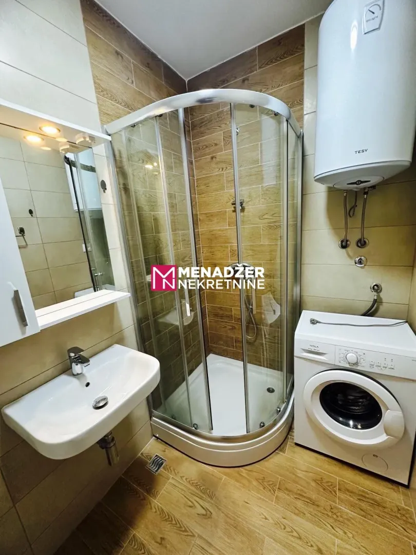 Small bathroom with a shower cabin, sink, and washing machine.