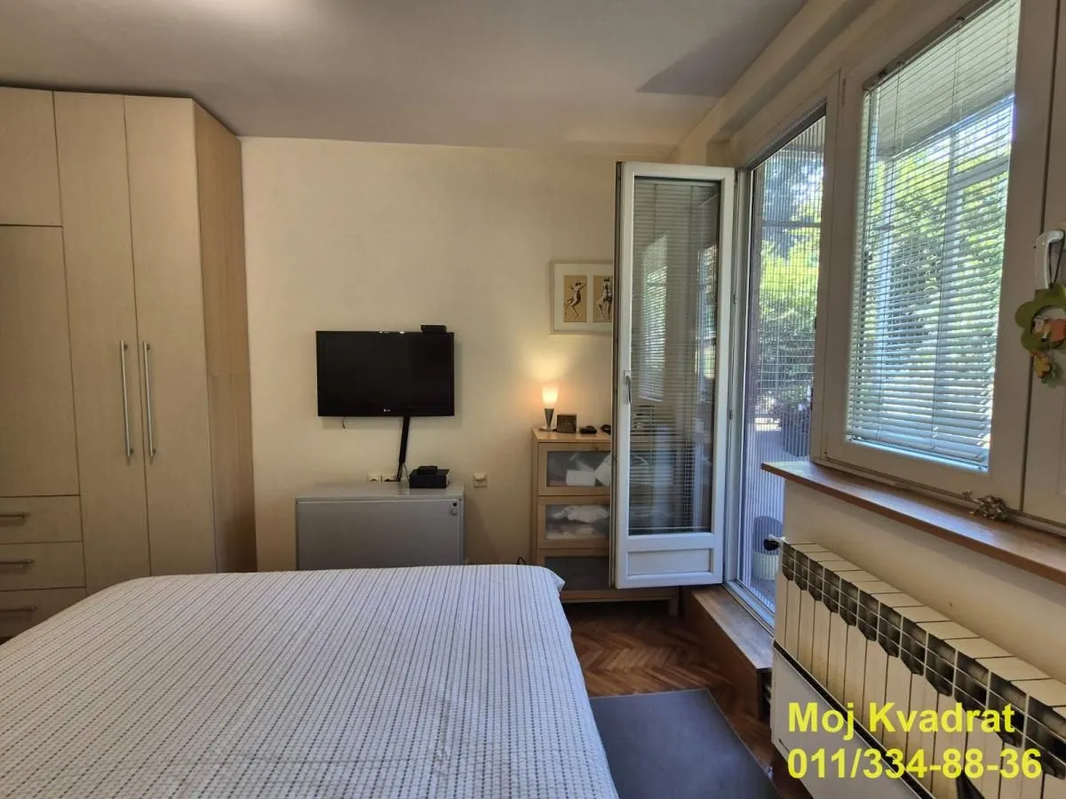 Nameštena spavaća soba sa bračnim krevetom, plakarom i izlazom na terasu.