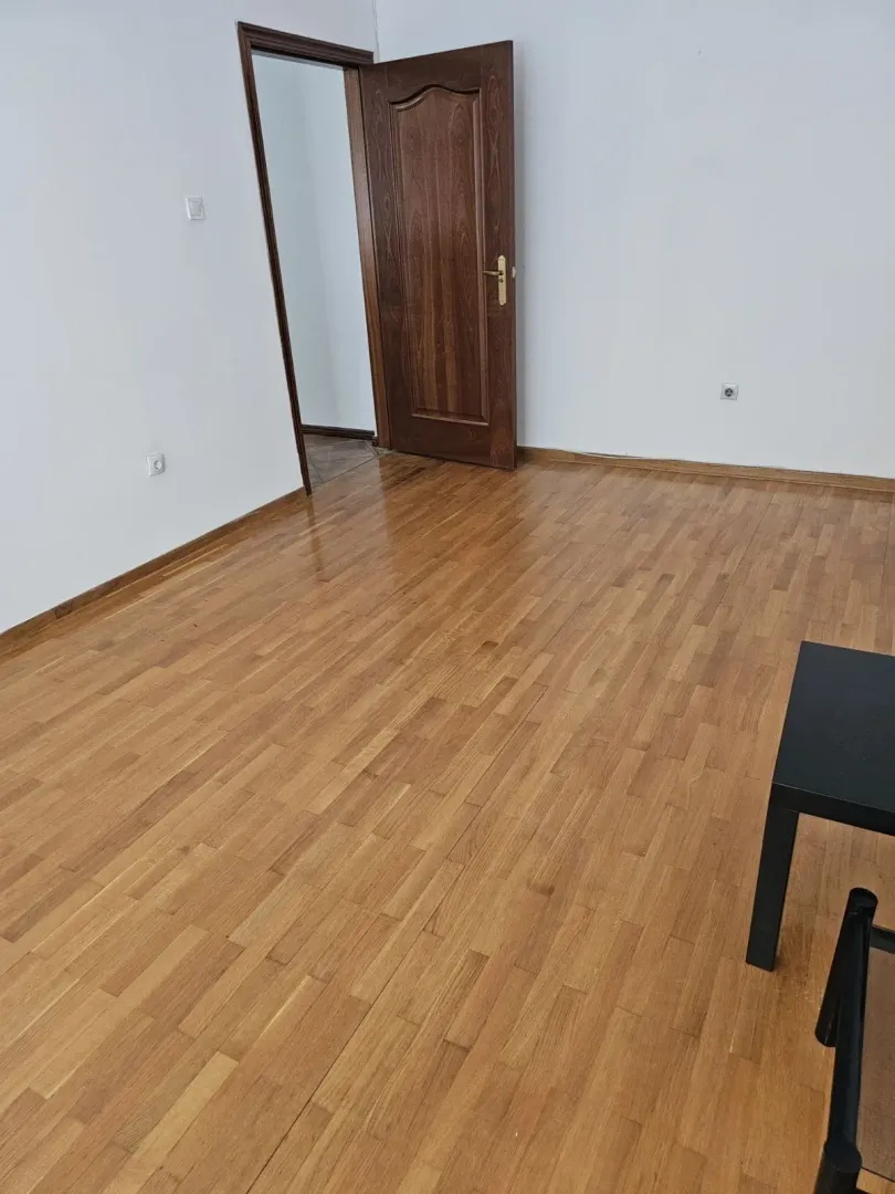 Prazna soba sa drvenim podom i otvorenim vratima.