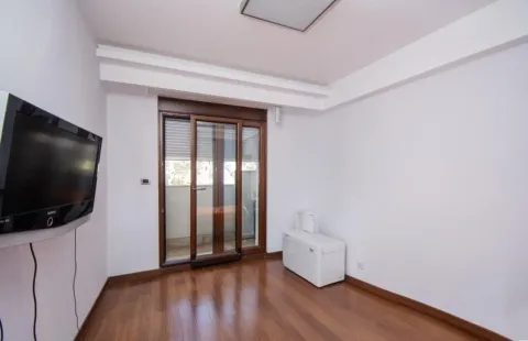Prazna soba sa drvenim podom, televizorom na zidu i balkonskim vratima. - image 4