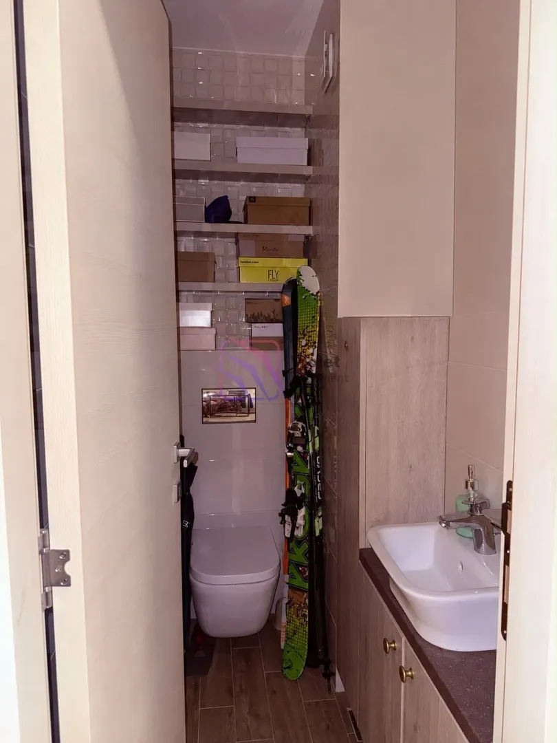 Manje kupatilo sa WC šoljom, umivaonikom i policama za odlaganje stvari.
