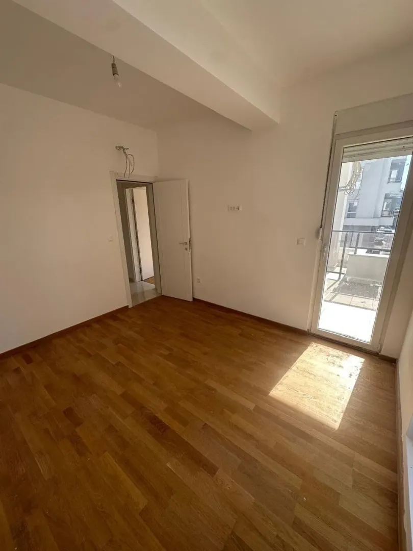 Prazna soba sa drvenim podom i izlazom na terasu.