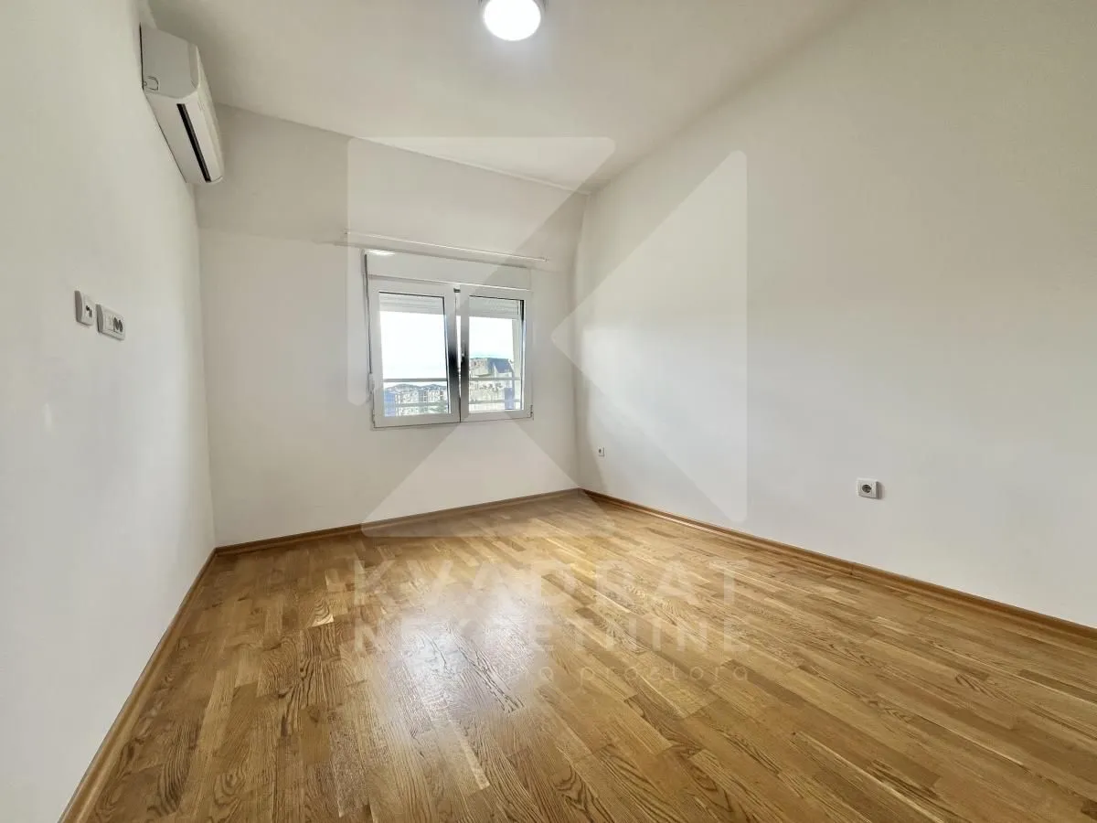 Empty room with wooden flooring, white walls, and an air conditioning unit.