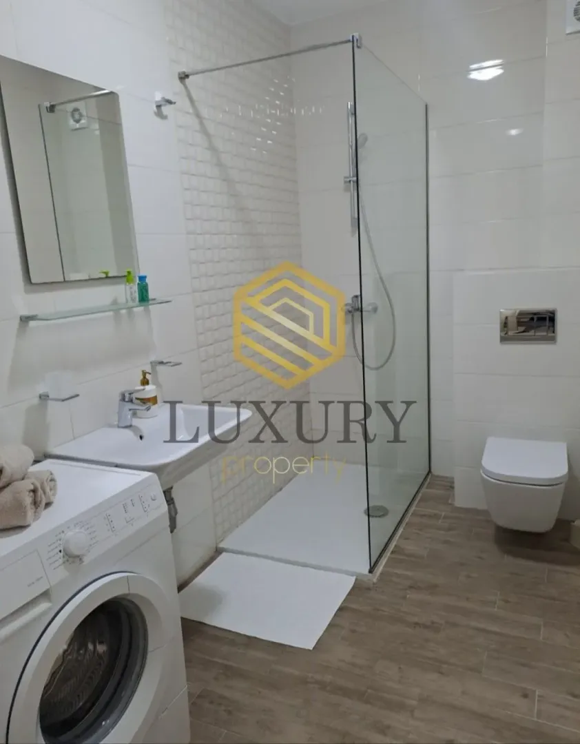 Modern bathroom with a walk-in shower, washbasin, toilet, and washing machine.