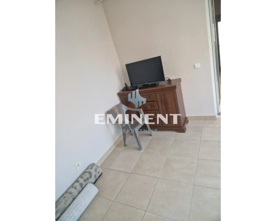 An empty room with a chest of drawers, a TV, and a rolled-up carpet on the floor.