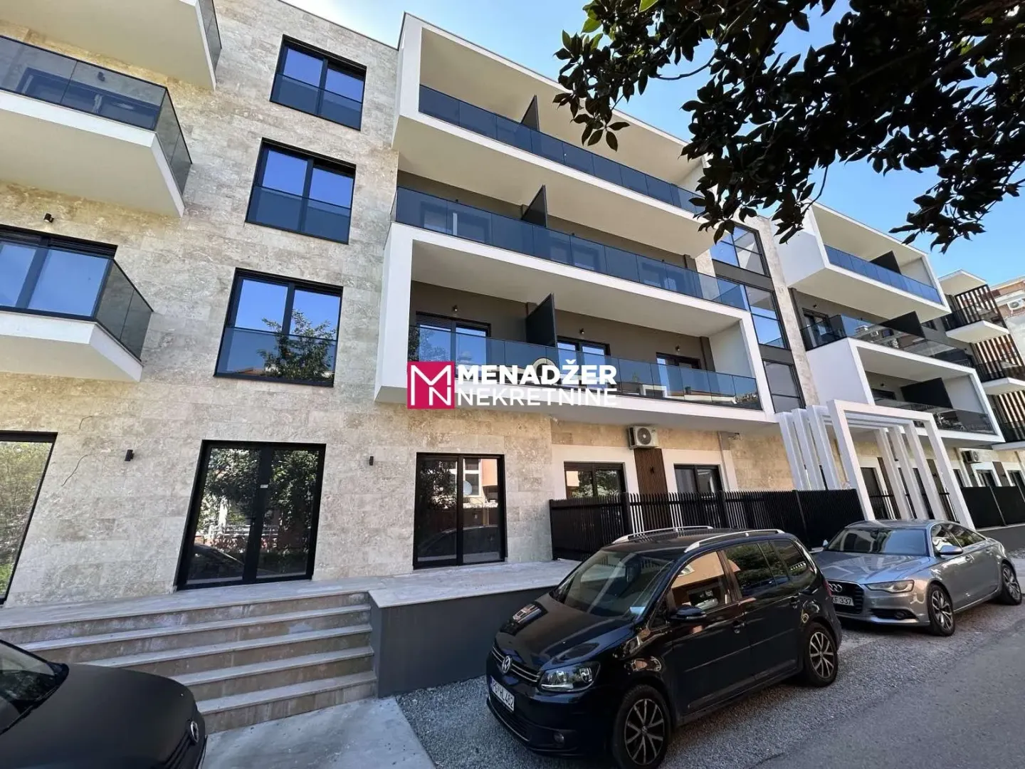 Exterior of a modern residential building with balconies and parked cars in front.