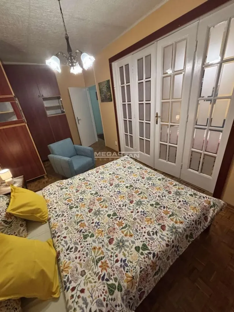 Furnished bedroom with a double bed, armchair, and wooden wardrobes.