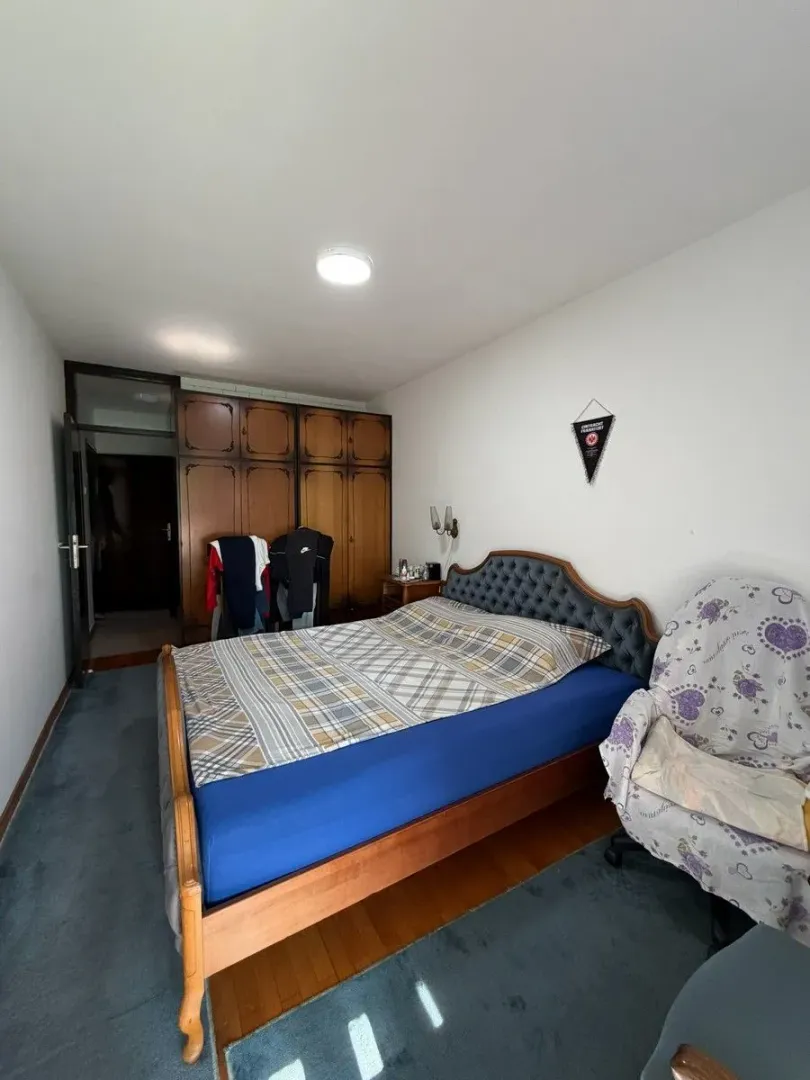 Spavaća soba sa bračnim krevetom, ormarom i foteljom.