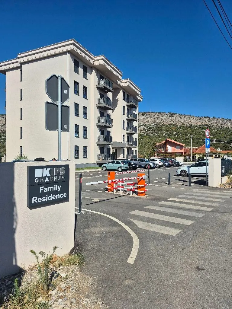 Pogled na spoljašnjost stambene zgrade i parking sa rampom.