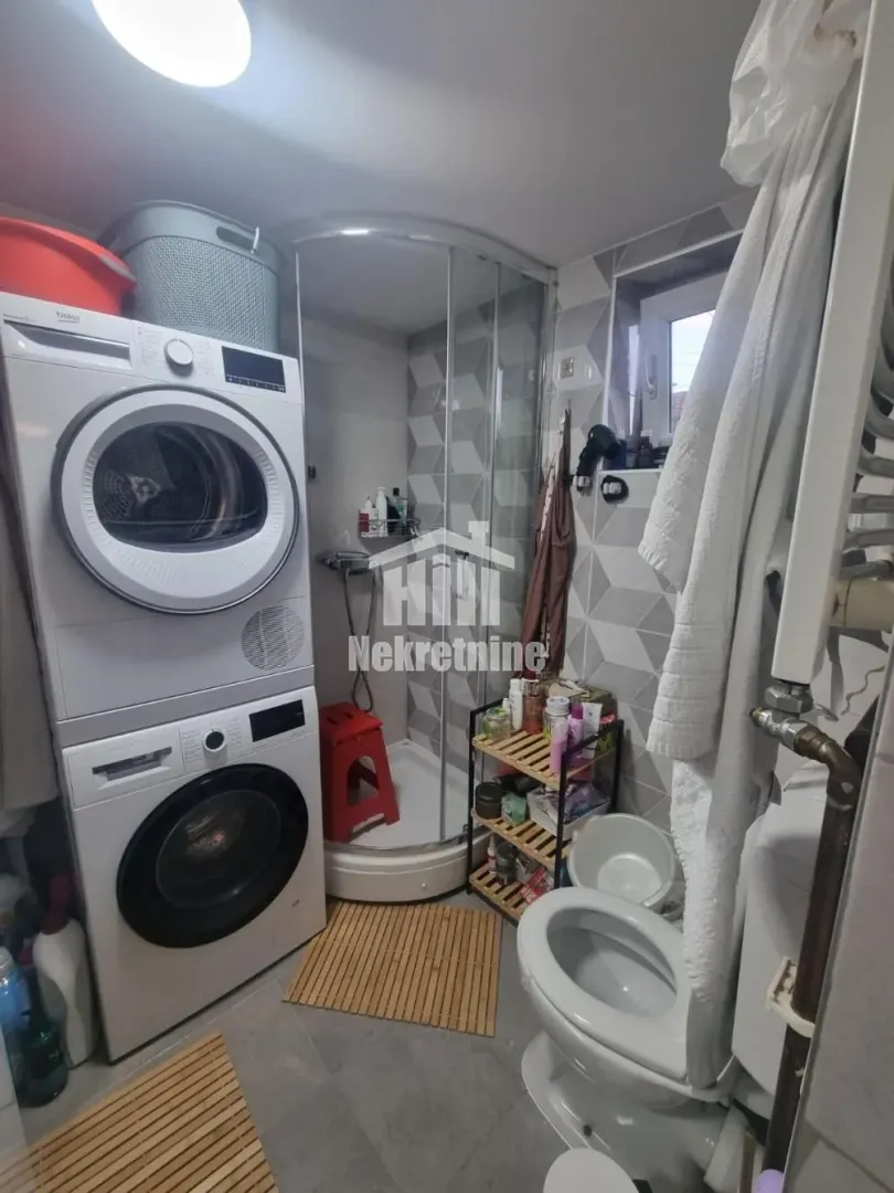 Kupatilo opremljeno tuš kabinom, WC šoljom i mašinama za pranje i sušenje veša.