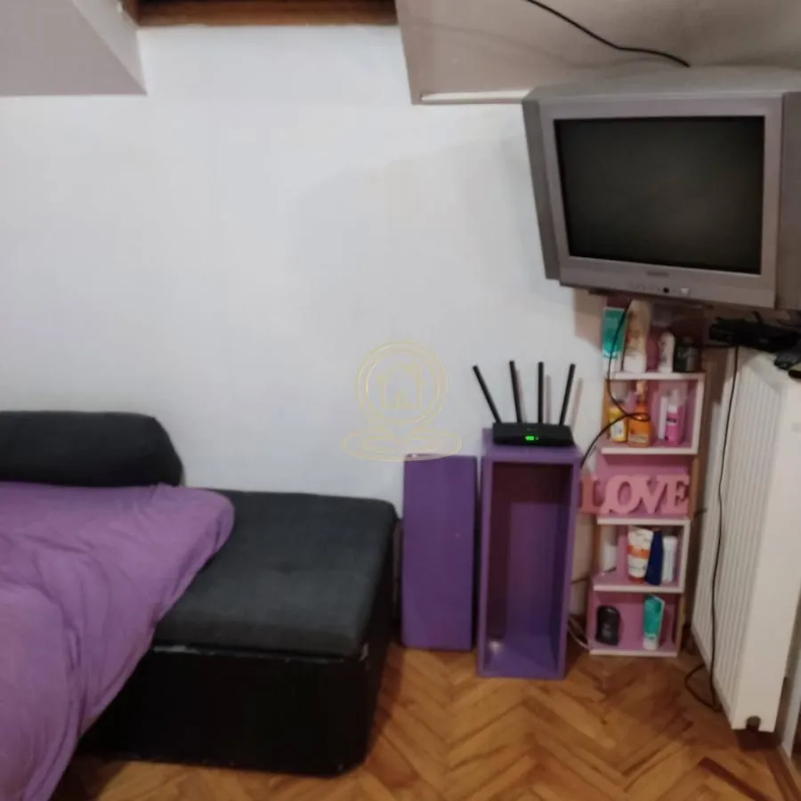 Deo spavaće sobe sa krevetom, TV-om i policom.