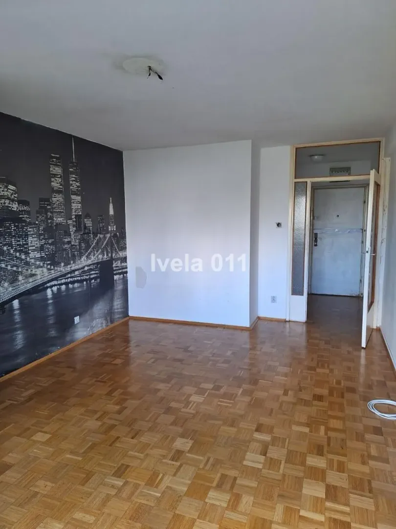 Empty living room with parquet flooring and a city motif wallpaper.