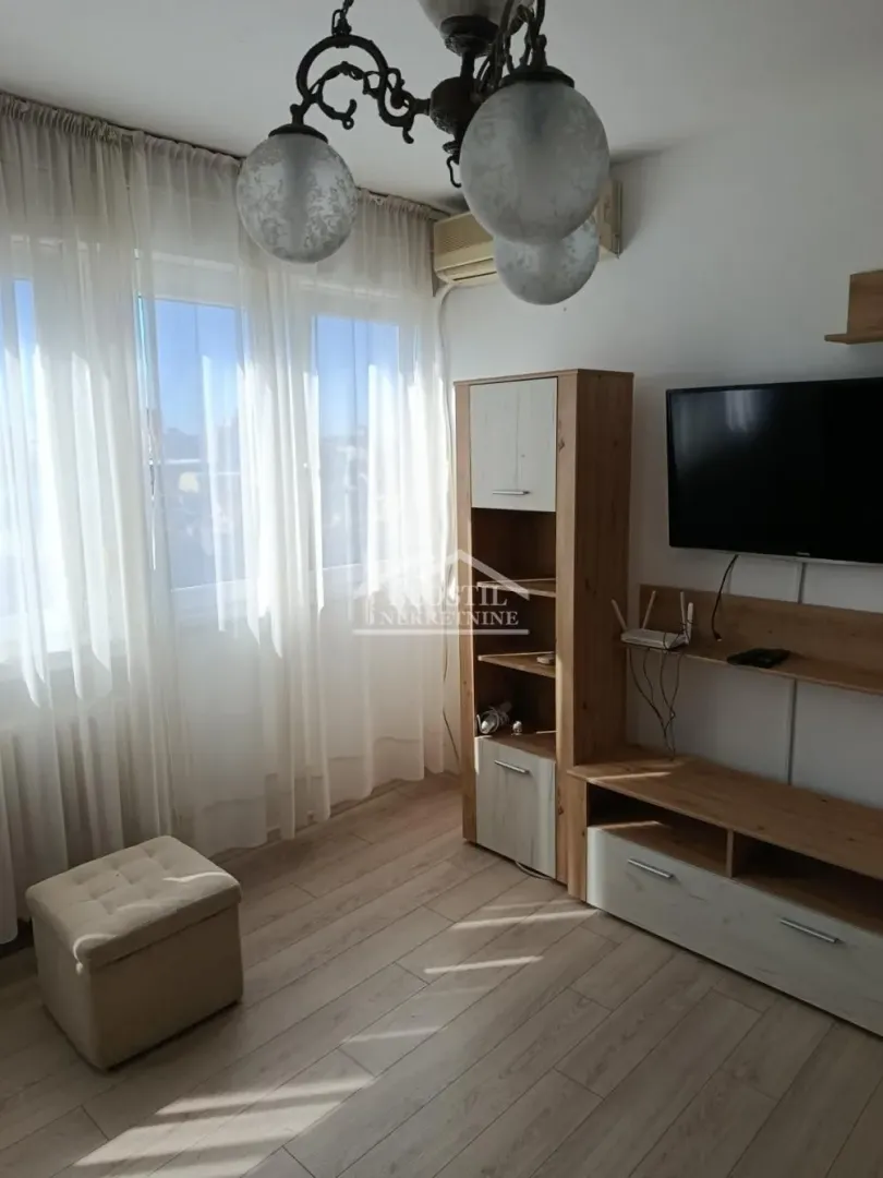 Dnevna soba sa TV komodom i prozorom prekrivenim zavesama.