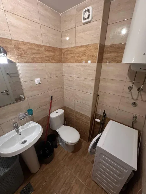 Smaller bathroom with a sink, toilet, water heater, and washing machine.