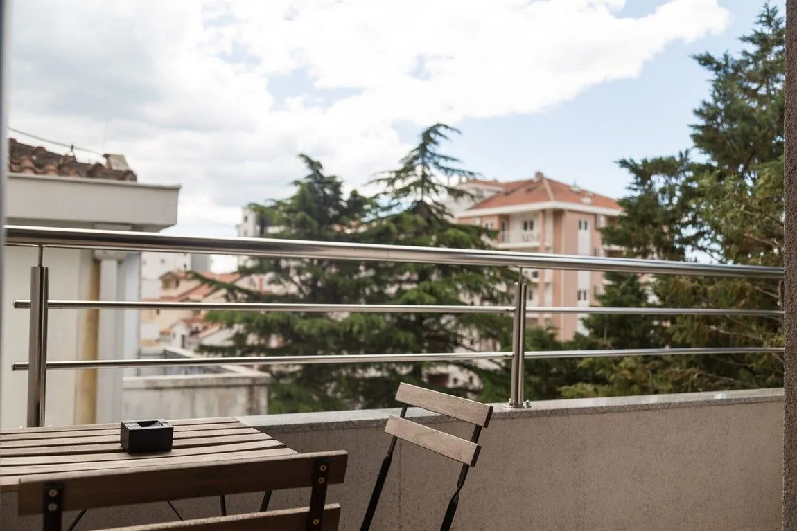 Manji balkon sa drvenim stolom, stolicama i metalnom ogradom.