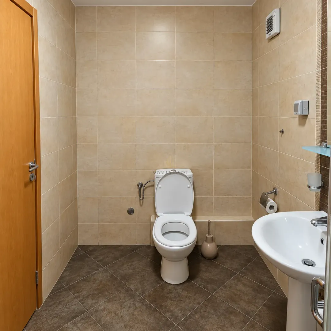 Kupatilo opremljeno WC šoljom, umivaonikom i pločicama u bež tonovima.