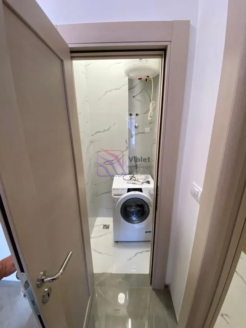 Pogled iz hodnika na manje kupatilo sa veš mašinom.