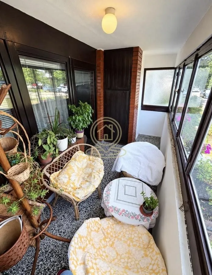 Enclosed balcony with seating furniture and houseplants.