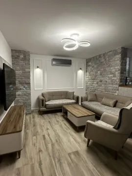 Dnevna soba sa garniturom za sedenje, TV komodom i dekorativnim kamenim zidom. - image 2