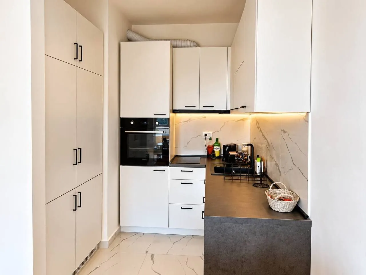 Modern white kitchen with dark countertops and built-in appliances.