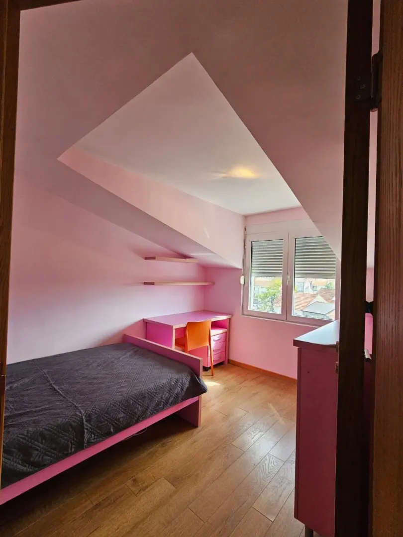Children's bedroom with a bed, desk, and slanted ceiling.