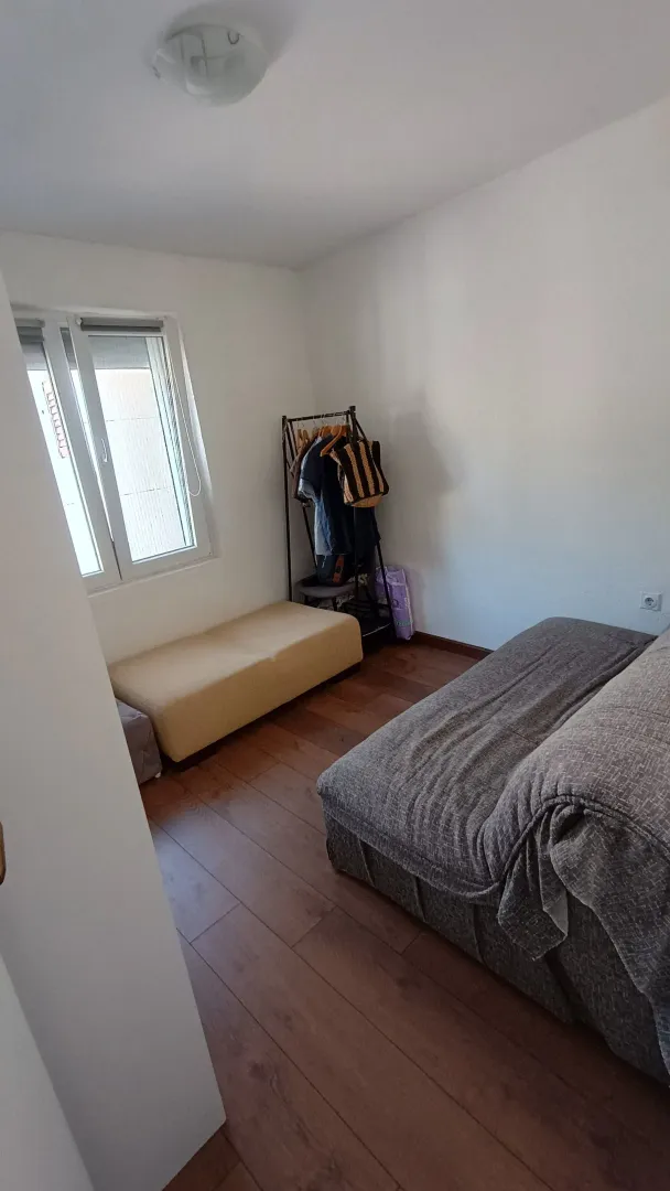Manja spavaća soba sa krevetom, foteljom i garderoberom pored prozora.