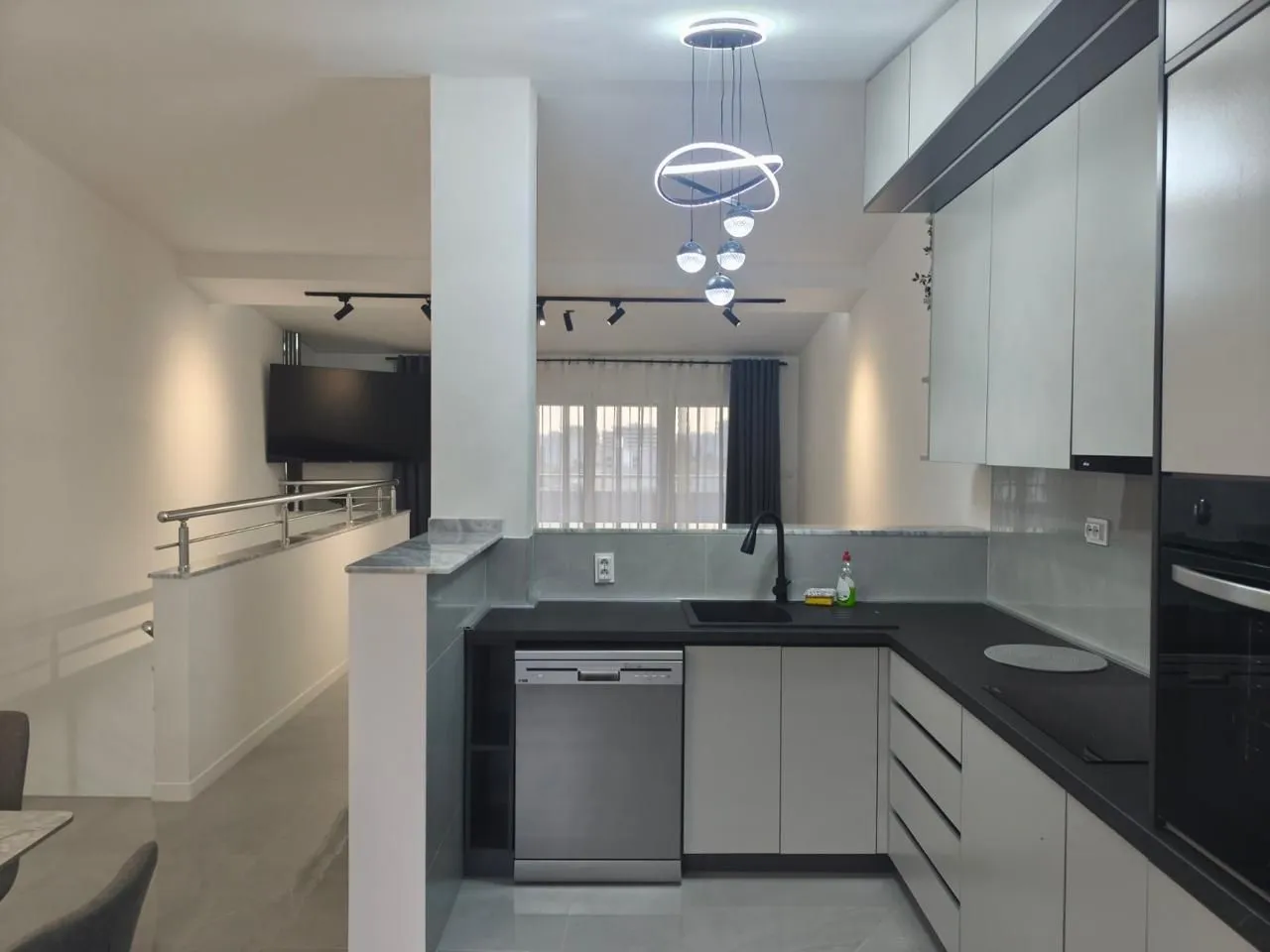 Modern kitchen with white cabinetry and black countertops, connected to the living area.