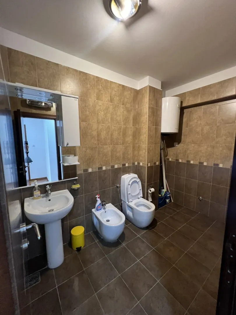 A bathroom with beige tiles, a sink, a bidet, and a toilet.