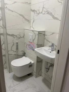 Small bathroom with white marble-patterned ceramic tiles, wall-hung toilet, and washbasin. - image 5
