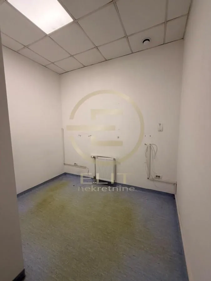 Empty office space with a dropped ceiling and radiator.