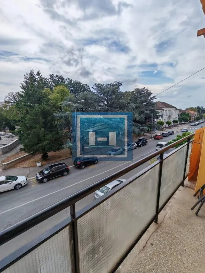 Pogled sa balkona na ulicu i drveće.