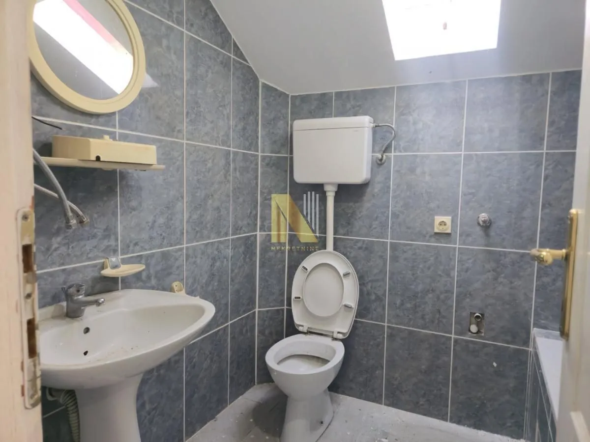 Kupatilo sa pločicama u sivoj boji, umivaonikom i WC šoljom.