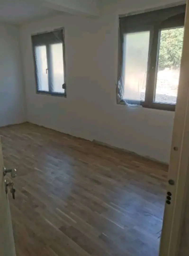 Prazna soba sa parketom i prozorima prekrivenim zaštitnom folijom.