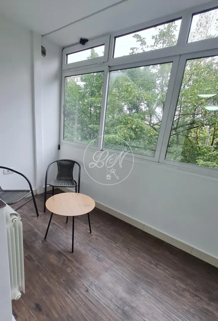 Enclosed balcony with a glass wall, small table, and chairs.