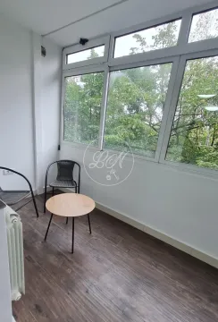 Enclosed balcony with a glass wall, small table, and chairs. - image 16