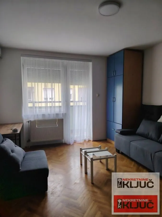 Dnevna soba sa garniturom za sedenje, plavim garderoberom i izlazom na terasu.