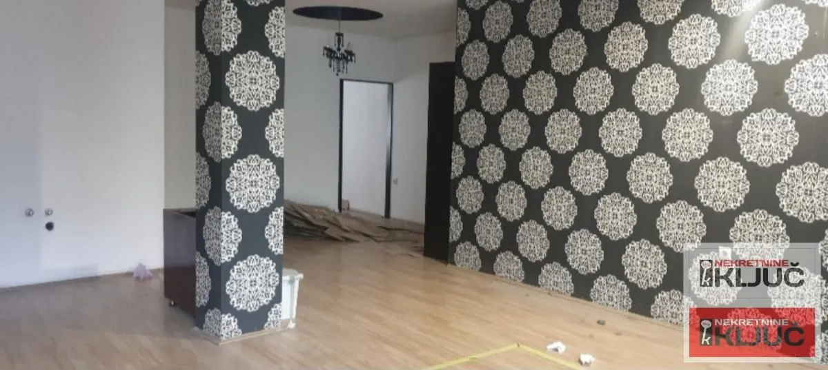 Empty living room with patterned wallpaper on the walls and laminate flooring.
