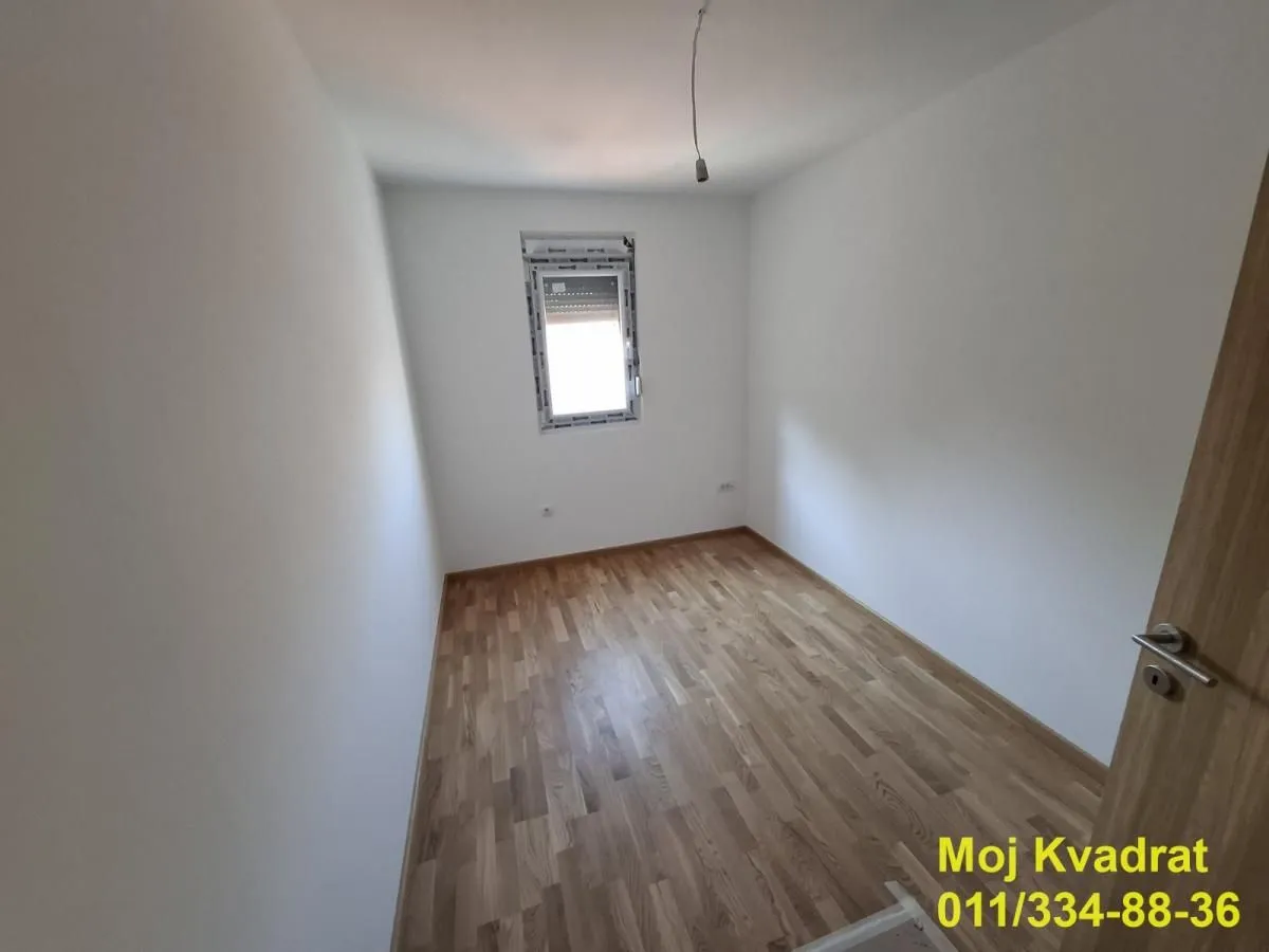 Prazna soba sa belim zidovima i drvenim parketom.