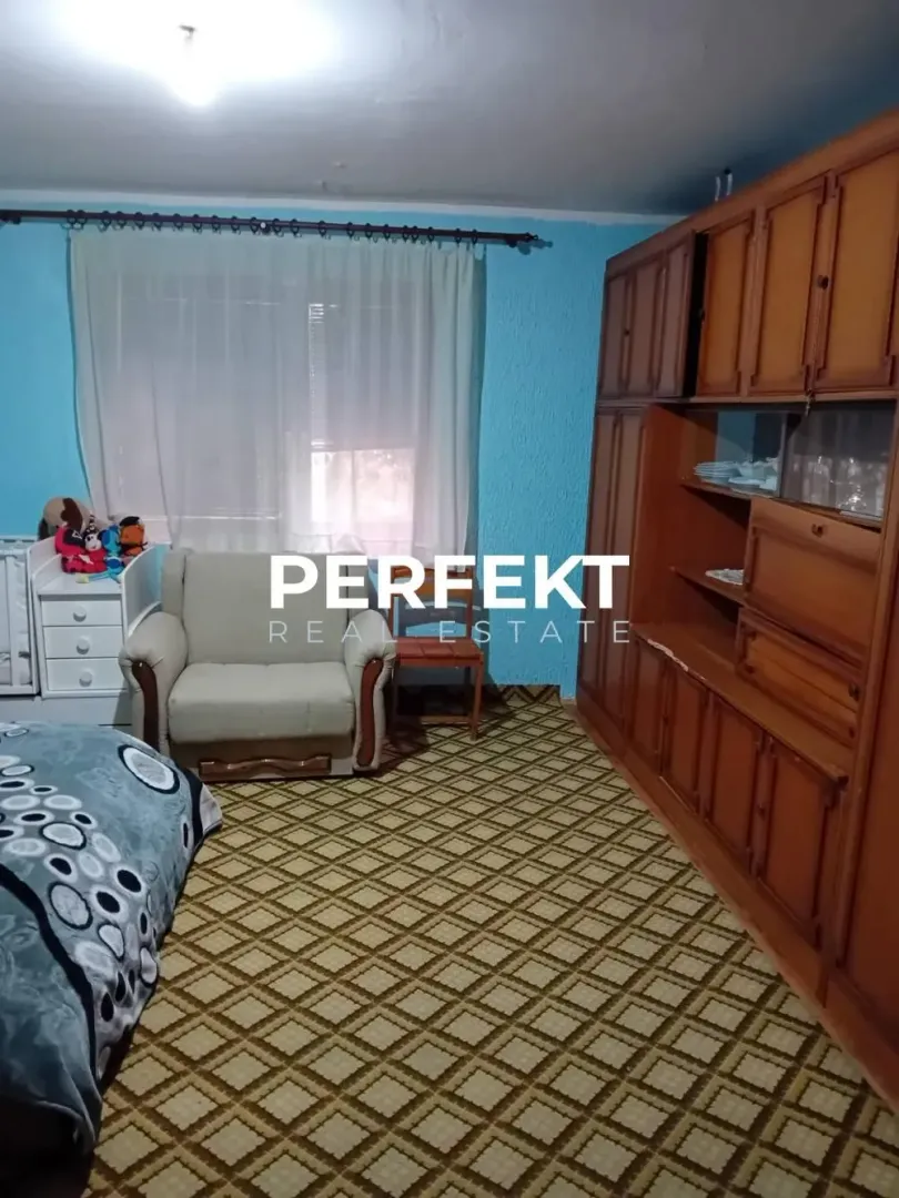 Nameštena spavaća soba sa krevetom, foteljom i velikim drvenim garderoberom.