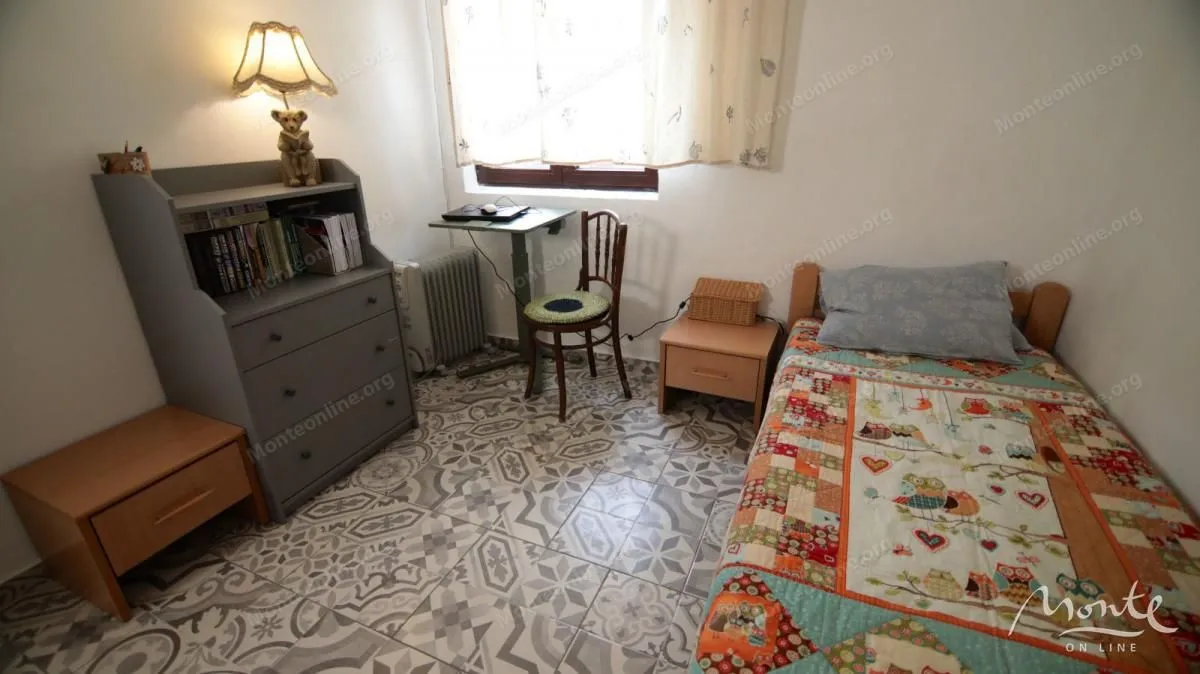 Manja spavaća soba sa krevetom, komodom i radnim stolom.