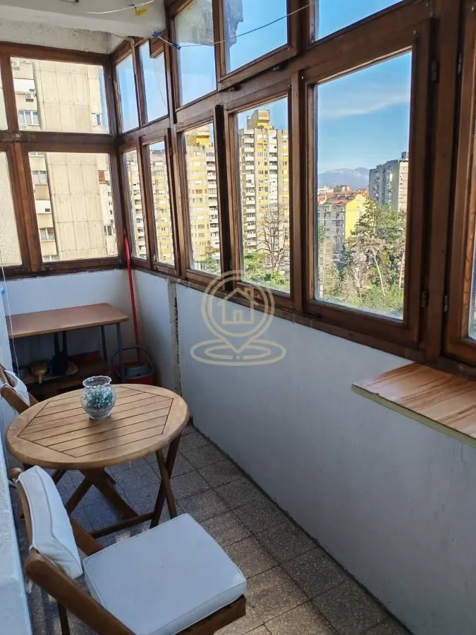 Enclosed balcony with wooden windows and sitting furniture.