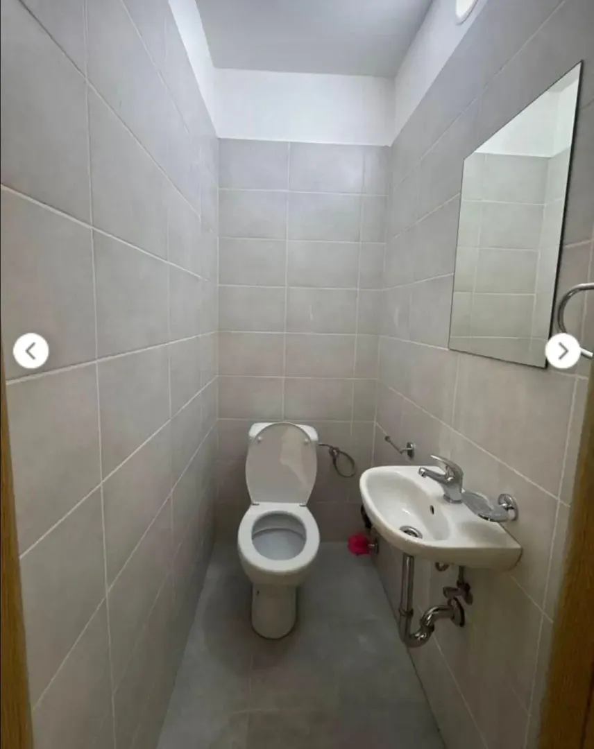 Small bathroom tiled in grey with a toilet, washbasin, and mirror.