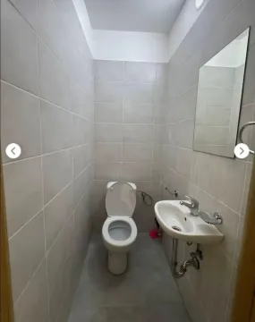 Small bathroom tiled in grey with a toilet, washbasin, and mirror. - image 3