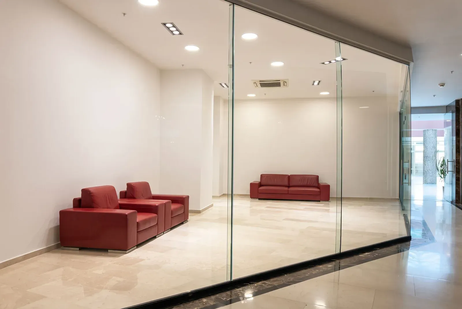 Modern office space with a glass partition and red leather sofas.