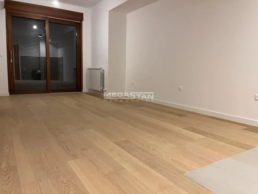 Empty room with wooden flooring and balcony doors.
